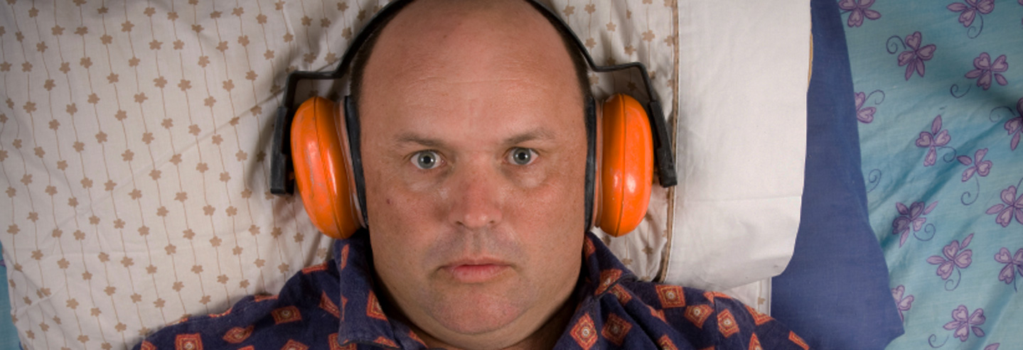 homme dans son lit contrarié et portant un casque anti-bruit