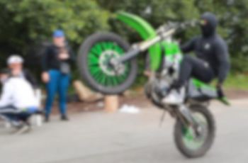 personne sur une moto verte et levant la roue regardee par d autres personnes